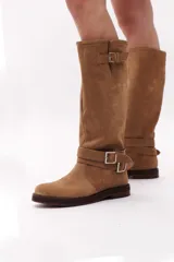 Bota de caña alta color marrón chocolate, confeccionada en gamuza. Presenta dos correas desmontables con hebillas metálicas plateadas.