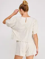 Blusa corta de lino y viscosa color beige, con bordado de grandes flores al tono, cuello redondo, mangas cortas abullonadas y corte holgado.