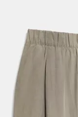 Pantalón fluido de tiro medio color verde militar, con cintura elástica en la parte trasera, pinzas en el delantero y bolsillos laterales ocultos en la costura. Presenta un diseño de pernera ancha y corte tobillero, con cierre frontal de cremallera y botón.