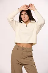 Buzo tejido de punto color beige, con cuello alto y cierre frontal parcial. Presenta mangas largas con diseño en tejido morley y corte holgado.