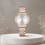 Reloj analógico de mujer con caja redonda y malla de eslabones metálicos en tono oro rosa. Presenta una esfera minimalista con índices brillantes y movimiento de cuarzo japonés.