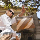 Sobre de mano de símil cuero con diseño de franjas diagonales en negro, blanco y marrón. Cuenta con cierre metálico frontal, bolsillo interior con cierre y otro abierto con división. Incluye correa desmontable para usar como bandolera.