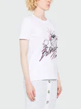 Remera de algodón blanca con cuello redondo y manga corta. Presenta un estampado frontal con diseño de piña y frutas, acompañado por el logo de Balmain Paris en tipografía cursiva con detalles en color rosado.