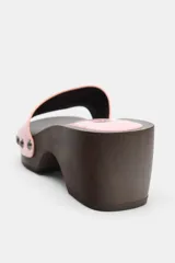 Sandalia de tacón tipo zueco con suela de madera oscura y plataforma, tira delantera ancha en material sintético rosa de efecto acharolado con tachas metálicas decorativas a los lados.