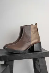 Bota corta de cuero negro con acabado combinado mate y charol. Presenta una tira decorativa con tachas metálicas y hebilla en el tobillo, tacón cuadrado robusto y suela con plataforma.