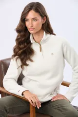 Buzo de polar color crema con cuello alto y cierre frontal parcial. Presenta detalles en cuero en el tirador del cierre y un pequeño bordado en el pecho y en la manga.