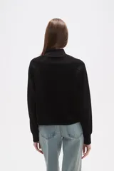 Buzo de manga larga color negro, con cuello alto tipo mock neck y corte holgado. Presenta costuras tipo raglán en los hombros.