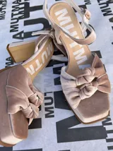 Sandalias de plataforma con taco alto cuadrado, confeccionadas en terciopelo color beige. Presentan un diseño con doble nudo en la parte frontal, puntera cuadrada y correa ajustable con hebilla en el tobillo.