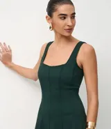 Vestido midi de corte evasé, color verde oscuro, con escote cuadrado, breteles anchos y recortes verticales que definen la silueta.