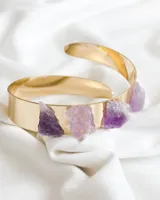 Brazalete rígido dorado con cuatro piedras amatistas irregulares incrustadas.