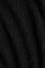 Vestido maxi negro sin mangas, de corte ajustado, con escote redondo y detalle de frunces drapeados en el lateral. El tejido presenta una textura sutilmente arrugada o gofrada.