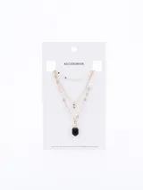 Collar de tres niveles en tono dorado, con cadenas de diferentes diseños, un dije pequeño con piedra brillante y un dije central en forma de punta de piedra negra.
