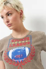 Remera negra de manga corta con estampa de escudo con la inscripción "Sports League" y una pelota de fútbol americano.