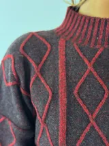 Sweater de lana color bordó con cuello alto y diseño de rombos y líneas verticales en rojo. Tiene puños y dobladillo acanalados.