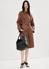 Chaqueta larga de efecto cuero color marrón, con cuello camisero, botonadura frontal oculta, bolsillos laterales y cinturón ajustable con hebilla en la cintura. Cuenta con trabillas en las muñecas y diseño amplio.