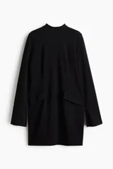 Vestido mini de manga larga confeccionado en punto interlock pesado. Presenta cuello mao, bolsillos delanteros decorativos con solapa y puños levemente acampanados con abertura. Incluye cierre oculto en la parte posterior.