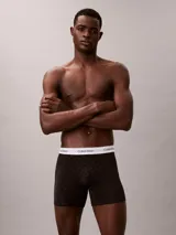 Pack de tres bóxers Calvin Klein tipo boxer brief de algodón elástico. Incluye un modelo negro con monograma estampado, uno azul oscuro liso y uno gris claro liso. Todos cuentan con cintura elástica blanca con el logo de la marca.