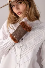 Camisa blanca de algodón con cuello alto, mangas largas abullonadas y cierre frontal de botones. Presenta un diseño delantero con alforzas y detalles de bordado inglés en forma de V.