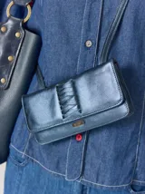 Cartera tipo bandolera de cuero metalizado en tono azulado, con diseño rectangular, solapa con cierre magnético y detalle de trenzado central. Incluye correa regulable y placa metálica con logo.