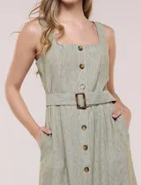 Vestido midi abotonado verde melange, con escote recto, tirantes anchos y falda de calce recto con vuelo sutil. Tiene abotonadura frontal completa con botones estilo carey, cinto textil con hebilla para ajustar la cintura y bolsillos laterales.