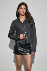 Campera de denim color negro con detalles de tachas metálicas en cuello, solapas, solapa de cierre y bolsillos frontales. Posee cierre frontal con botones metálicos y bolsillos con solapa en el pecho.
