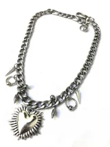 Collar plateado de cadena gruesa con dije de corazón con rayos y detalles de piercing.