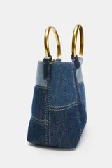 Bolso de hombro tipo mini saca con cuerpo en patchwork de denim en tonos azules. Posee una anilla metálica dorada como asa de mano y una correa bandolera extraíble.