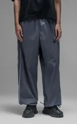 Pantalón deportivo de corte regular confeccionado en microfibra opaca, con cintura elástica y puños ajustables en los tobillos. Presenta vivos laterales a contratono que recorren toda la pierna y un pequeño parche con logo en el frente.