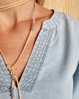 Blusa celeste de mangas 3/4 abullonadas, escote en V con detalle de bordado y lazo decorativo.