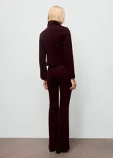 Pantalón jeans flare de terciopelo color bordó, de tiro alto y diseño largo, con cinco bolsillos, trabillas para cinturón y cierre frontal con botón y cremallera.