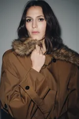 Trench largo color marrón, de corte amplio, con cuello solapa desmontable de pelo sintético marrón. Presenta cierre cruzado con botones oscuros y cinturón de tela anudado a la cintura.