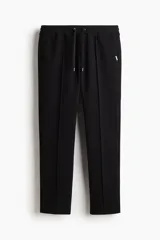 Jogging sastrero color negro de corte regular, confeccionado en mezcla de algodón de peso medio. Cuenta con cintura elástica con cordón ajustable, bolsillos laterales y pliegues delanteros cosidos.