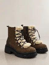 Bota tipo borcego de cuero color marrón, con suela track de goma negra. Presenta un aplique frontal desmontable de textil tipo corderito en color crema, con cordones negros y ganchos metálicos.