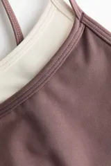 Top deportivo color malva con forro interior en tono crudo, confeccionado en tejido funcional con diseño de doble bretel fino en contraste y copas con relleno extraíble.