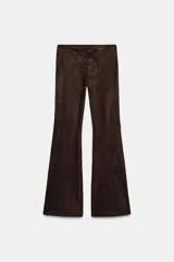 Pantalón de tiro bajo confeccionado en gamuza marrón, con diseño flare y detalle de lazada frontal. Presenta costuras marcadas y cierre lateral con cremallera.