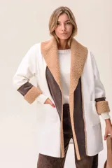 Saco de corte largo en color blanco, con solapas amplias y puños decorados con textura de corderito en color tostado. Presenta detalles en cuero sintético marrón en la parte frontal y en los puños, además de bolsillos laterales.