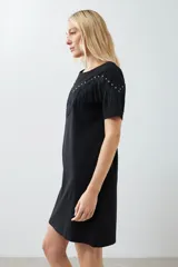 Vestido corto negro con cuello redondo, mangas cortas y detalle de flecos en el pecho.