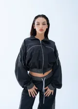 Campera rompeviento negra de estilo deportivo, con cierre frontal completo, cuello alto y detalles de líneas blancas en los hombros y mangas. Presenta puños y cintura elásticos en tono gris oscuro.