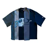 Remera de corte boxy fit, confeccionada con un diseño de paneles verticales en tonos negro y gris. Presenta una estampa frontal con el rostro de una mujer, letras y gráficos abstractos.