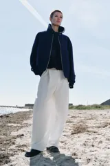 Chaqueta bomber de corte holgado confeccionada en tejido con lana, color azul marino. Presenta cuello subido, cierre frontal con cremallera metálica, bolsillos delanteros y detalle de trabillas con botones metálicos en el ruedo.