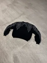 Sweater negro con cuello redondo y diseño geométrico en gris en la parte superior del pecho y hombros.