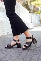 Sandalias negras de cuero con dos tiras, una de cuero liso y otra de charol con estampado animal print. Tienen hebilla metálica plateada y taco bloque.