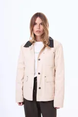 Campera de gabardina color beige con cuello de cuero sintético negro, cierre frontal con botones metálicos y bolsillos frontales con solapa.