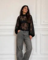 Blusa negra de encaje transparente, con cuello alto y mangas largas abullonadas estilo globo con puños ajustados.