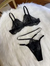 Conjunto de lencería de cuatro piezas en encaje negro. Incluye bralette con breteles regulables, tanga con tiras dobles ajustables en la cintura, portaligas con enganches desmontables y ligas para las piernas.