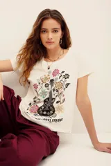 Remera blanca de algodón con cuello redondo, mangas cortas y estampa frontal de una guitarra rodeada de flores y la frase 'your own muse'.