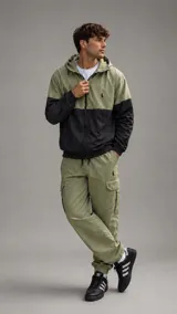 Conjunto deportivo de nylon compuesto por una campera con capucha y cierre frontal, con diseño bicolor en verde oliva y negro, y un pantalón cargo a juego en color verde oliva con bolsillos laterales y puños elásticos.