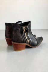 Bota corta de cuero negro con diseño combinado, punta fina y taco geométrico de madera. Presenta detalles en textura croco, apliques laterales con cierre, detalles metalizados y talón con acabado texturizado.