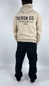 Canguro color tostado con capucha, corte oversize y estampado en la espalda con la leyenda "DUXON CO.", texto en japonés y "TOKYO".