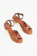 Sandalia de cuero vacuno color suela con diseño calado en la capellada y en la tira del tobillo. Presenta un taco bloque de madera y cierre con hebilla metálica.